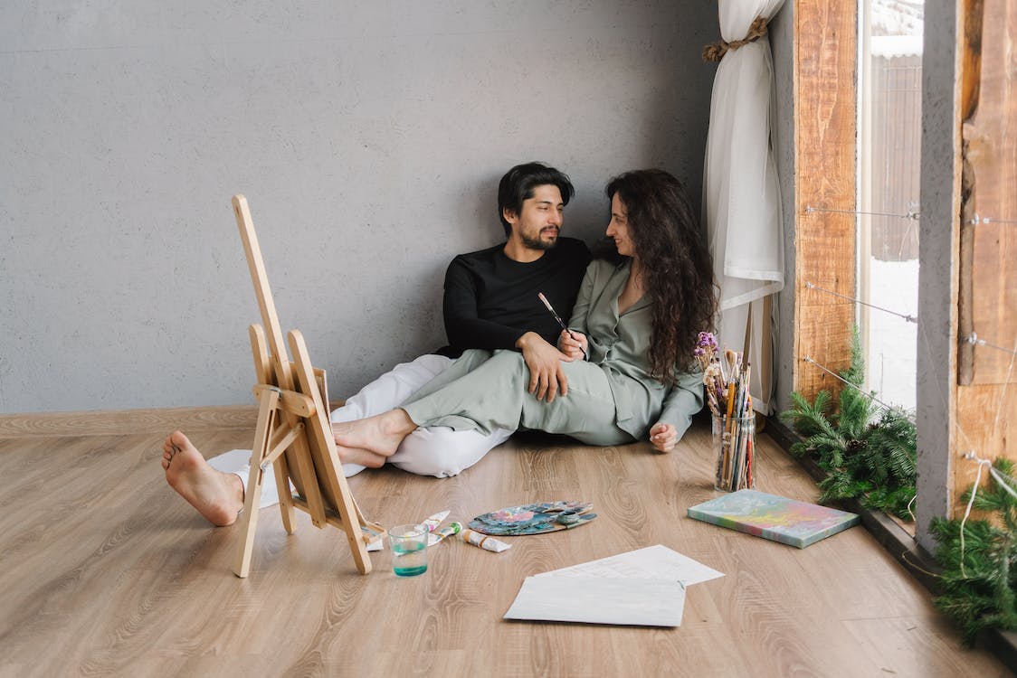 Couple sitting on the floor after painting session with art supplies being on the floor