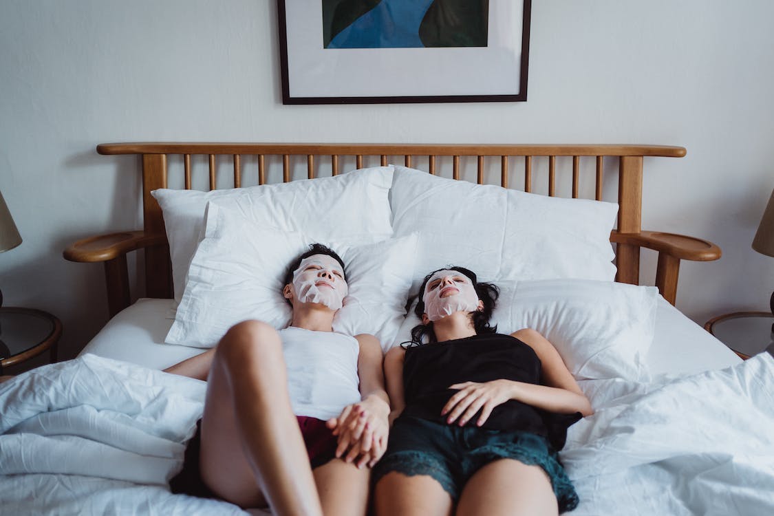 Couple laying on the bed with face masks, holding hands
